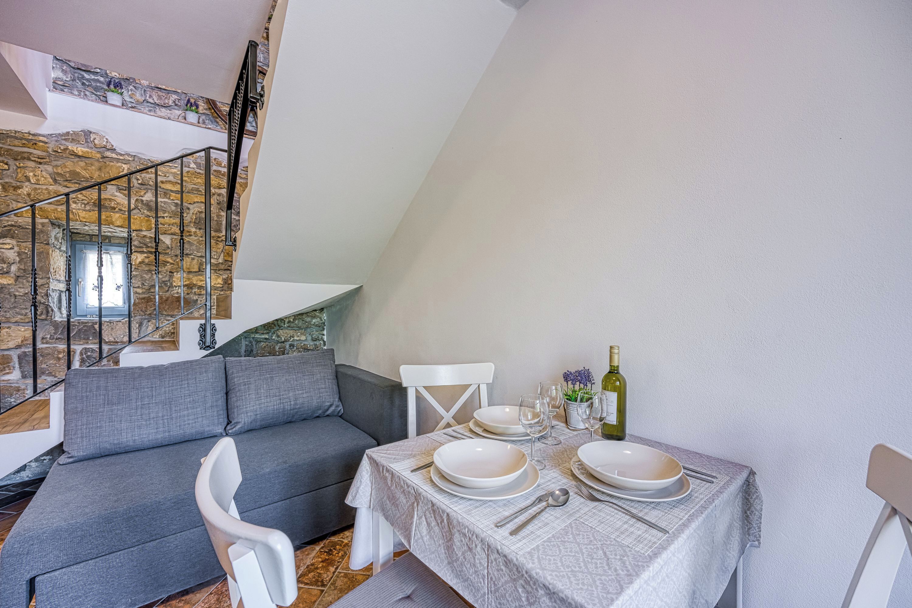 Un comedor con una mesa lista para cuatro personas, un sofá y una escalera con paredes de piedra.