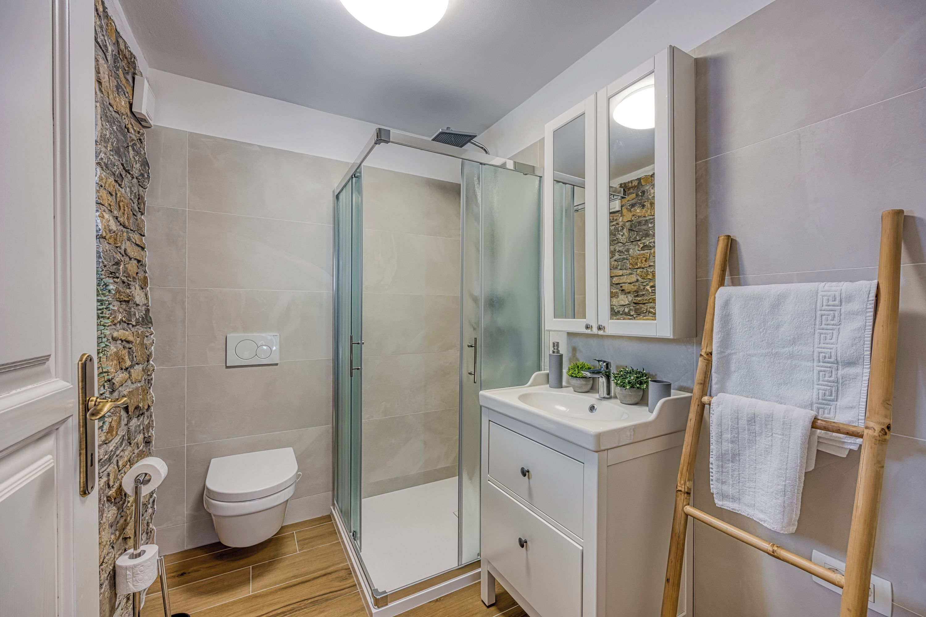 A bathroom with a glass shower enclosure, a toilet, a sink with a mirror, and a towel rack.