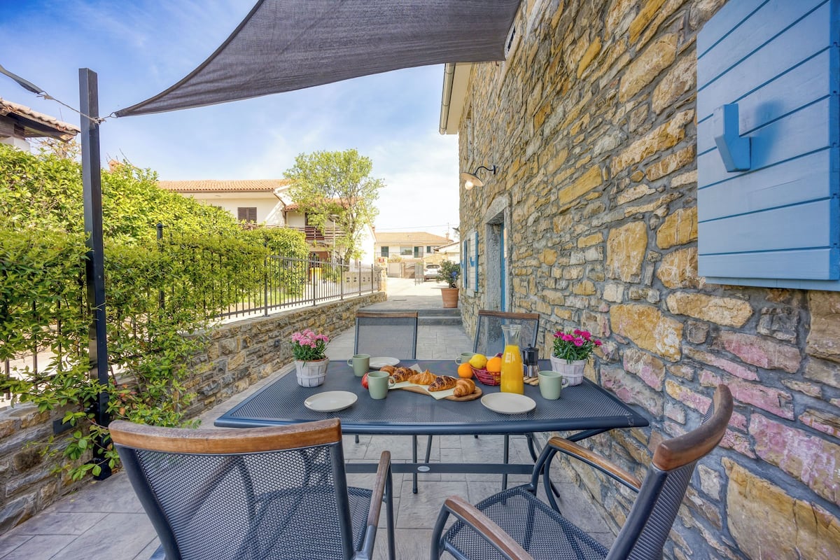 An outdoor dining area with a table set for breakfast, surrounded by stone walls and a shaded umbrella.