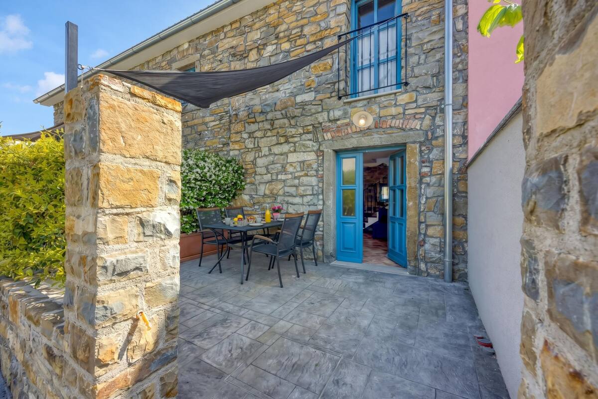 A stone building with a balcony, a table with chairs, and a door.