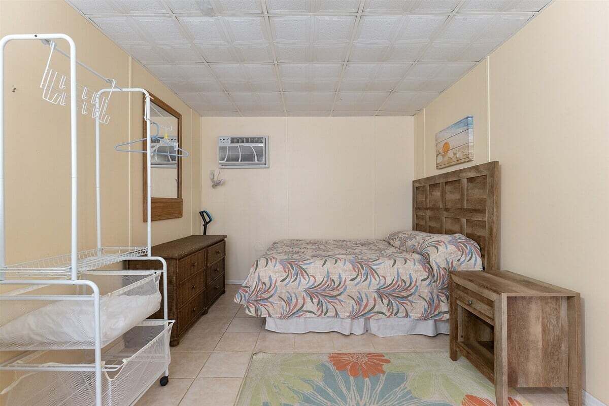 A bedroom with a bed, a dresser, a nightstand, a wall-mounted air conditioner, and a ceiling fan.