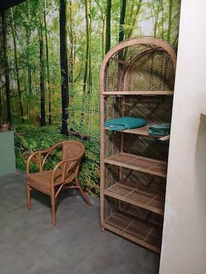 Une pièce avec un fauteuil en osier, une étagère en matériaux tressés et une fresque murale sur le thème de la forêt.