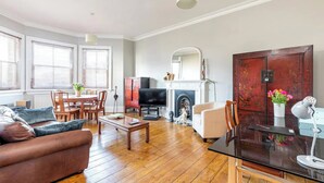 A living room with a sofa, coffee table, TV, fireplace, and dining area. - Spacious Central Hove Beach Flat (Hove)