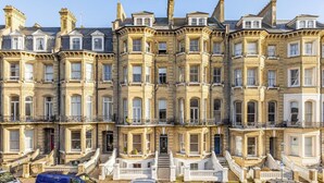 A row of terraced houses with uniform architecture, featuring bay windows and a central entrance with steps. - Spacious Central Hove Beach Flat (Hove)
