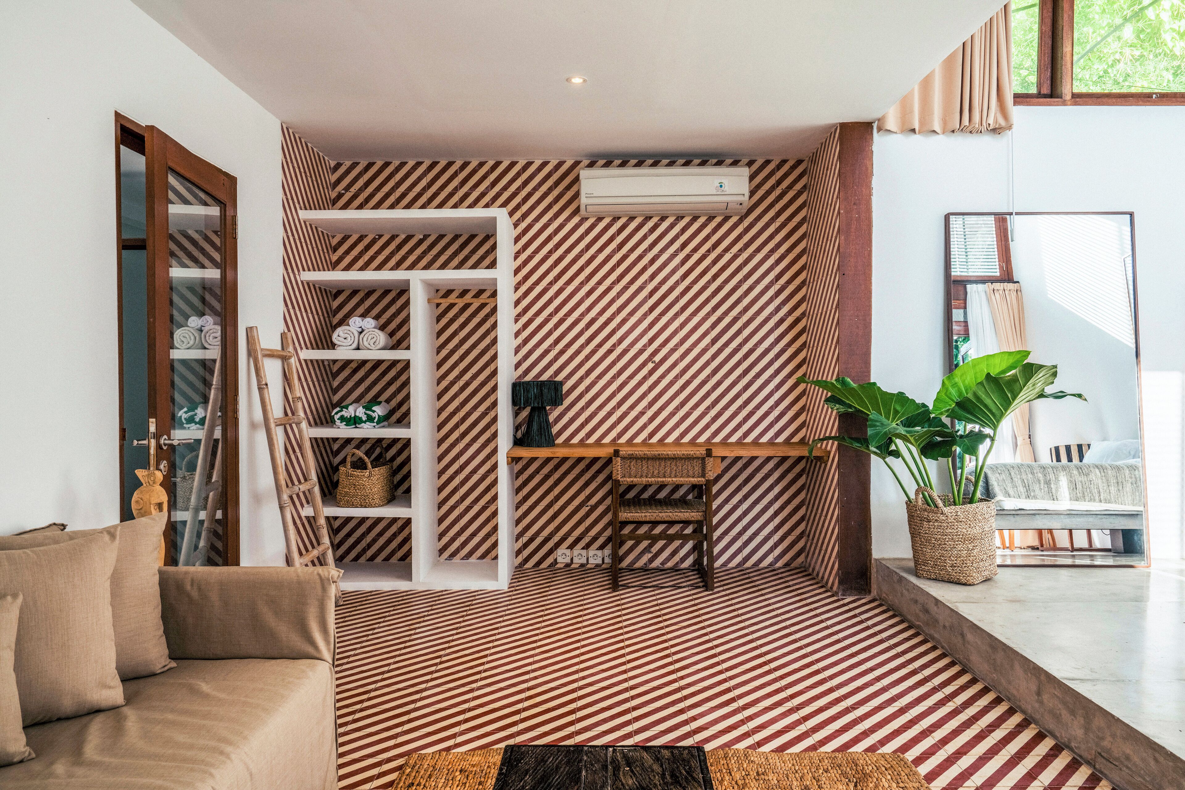 A room with a striped floor, a sofa, a small table, a chair, a shelf with towels, and a potted plant.
