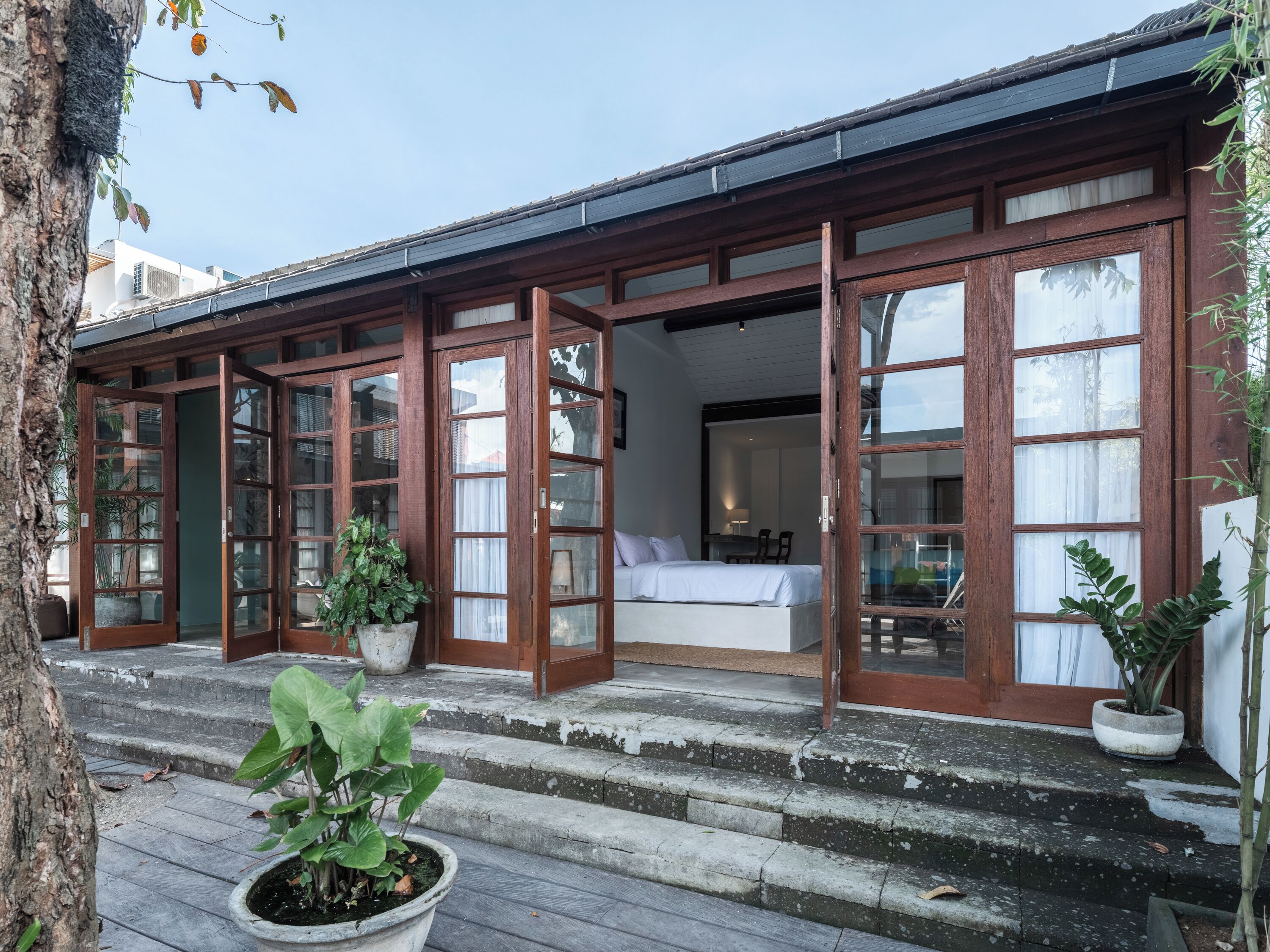 A traditional wooden building with large glass doors leading to a bedroom with a bed and a desk.