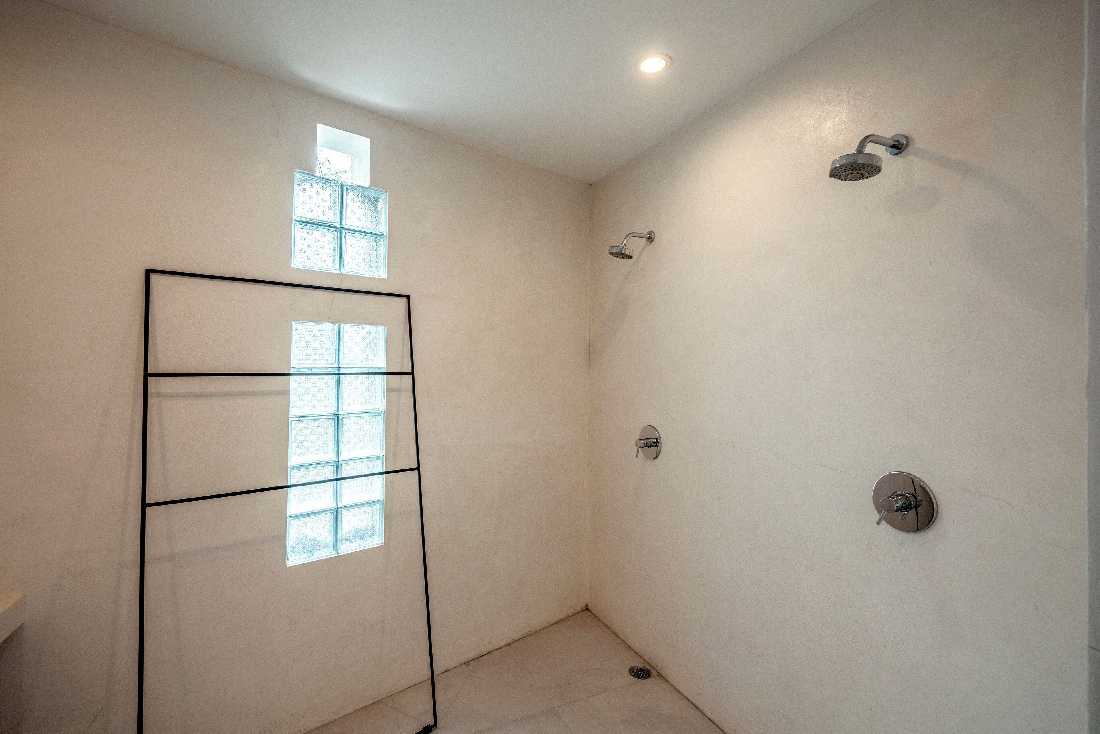 A small, white-walled bathroom with a shower, a window, and a towel rack.