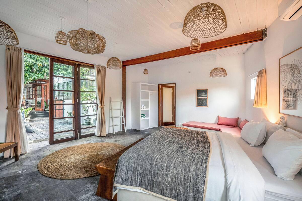 Ruime slaapkamer met een groot bed, een bankje en uitzicht op een houten terras door een schuifdeur van glas.