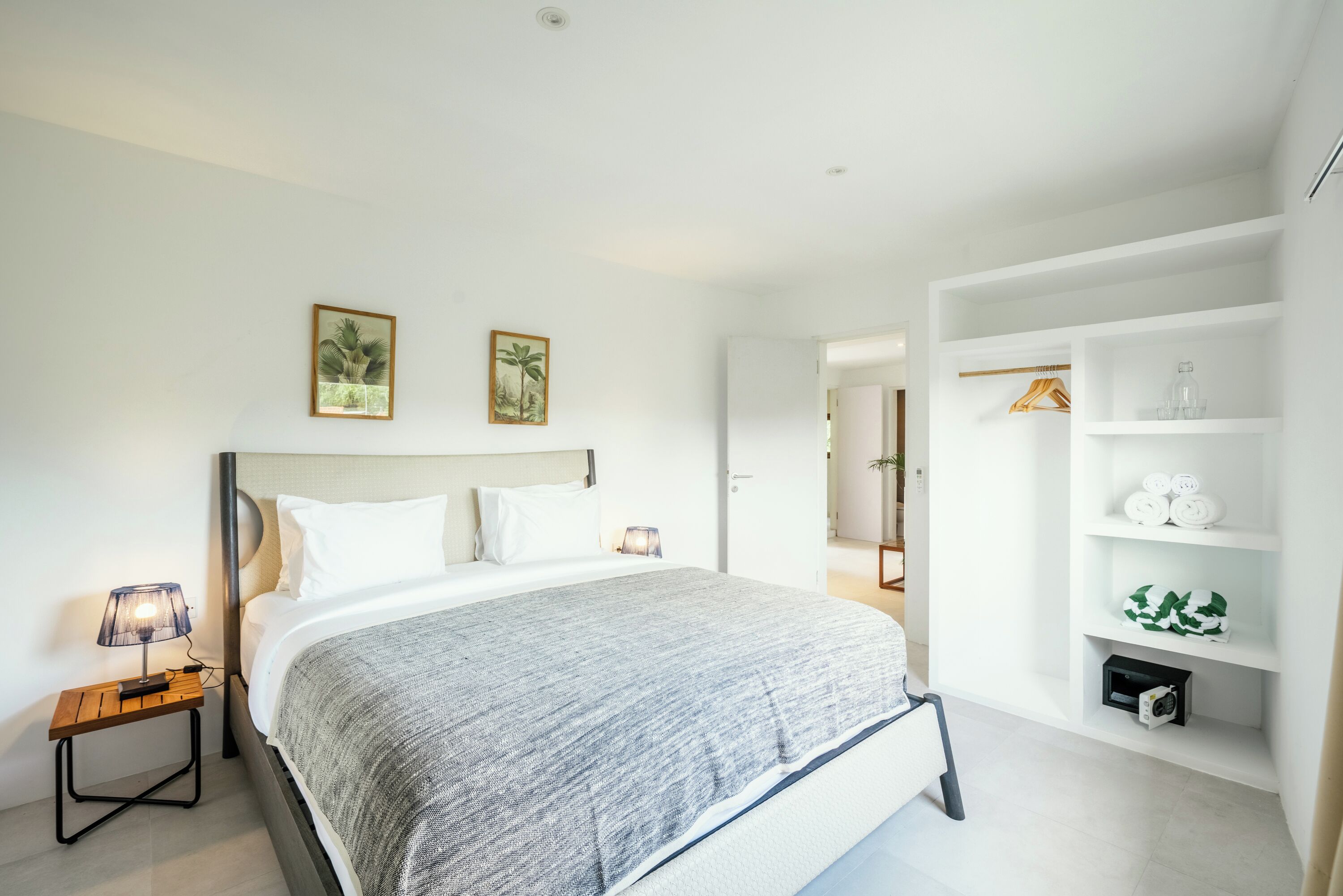 A modern bedroom with a large bed, a bedside table with a lamp, and a built-in wardrobe with shelves.