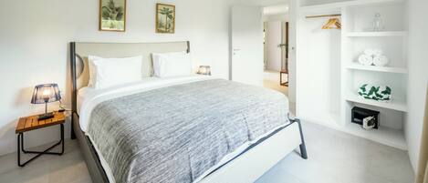 A modern bedroom with a large bed, a bedside table with a lamp, and a built-in wardrobe with shelves.