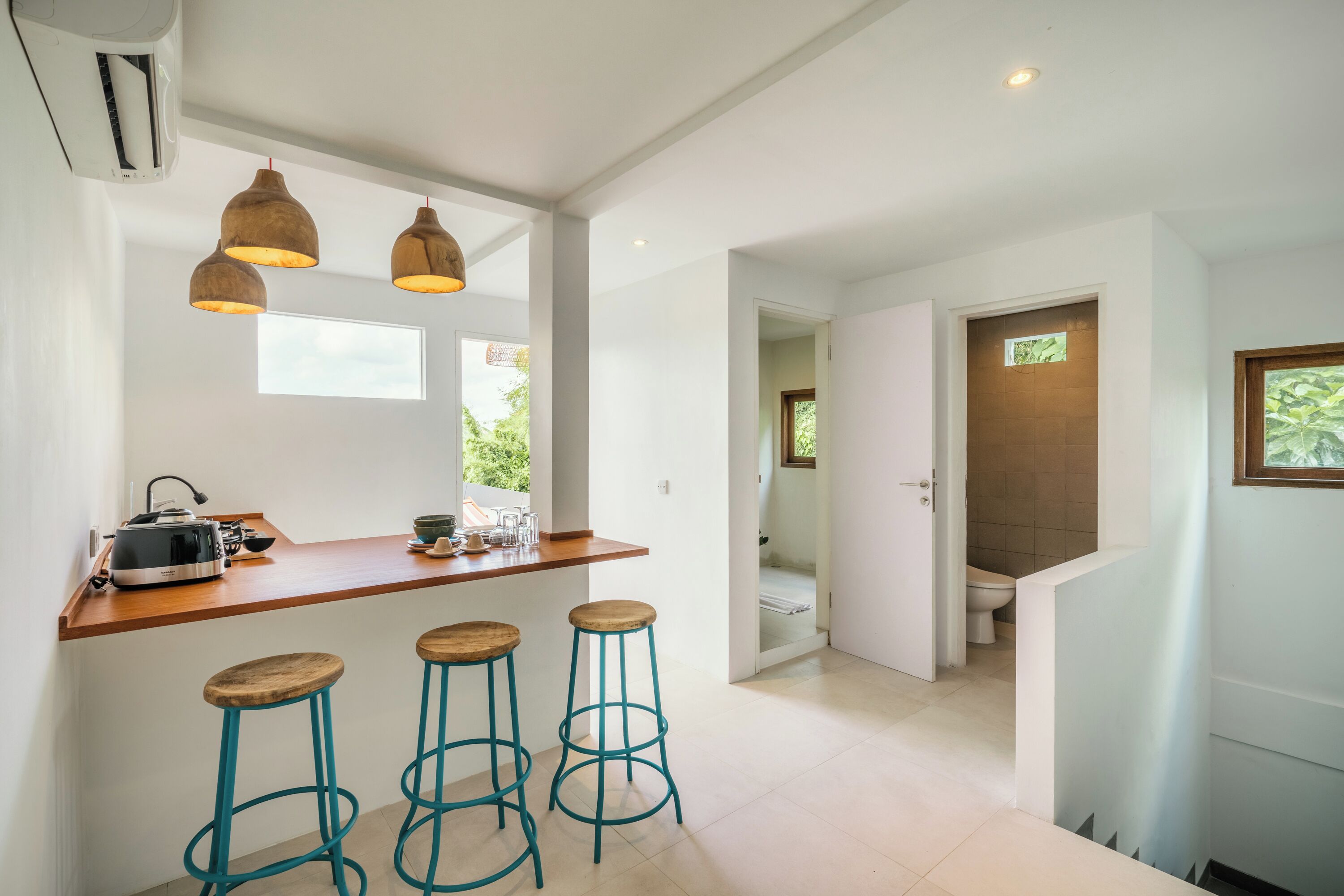 A modern kitchen with a wooden countertop, three stools, and pendant lighting.