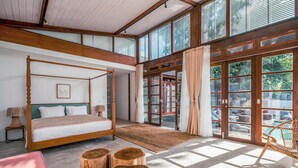 Ein geräumiges Schlafzimmer mit Himmelbett, Holz-Nachttischen und einem großen Fenster mit Blick ins Freie.