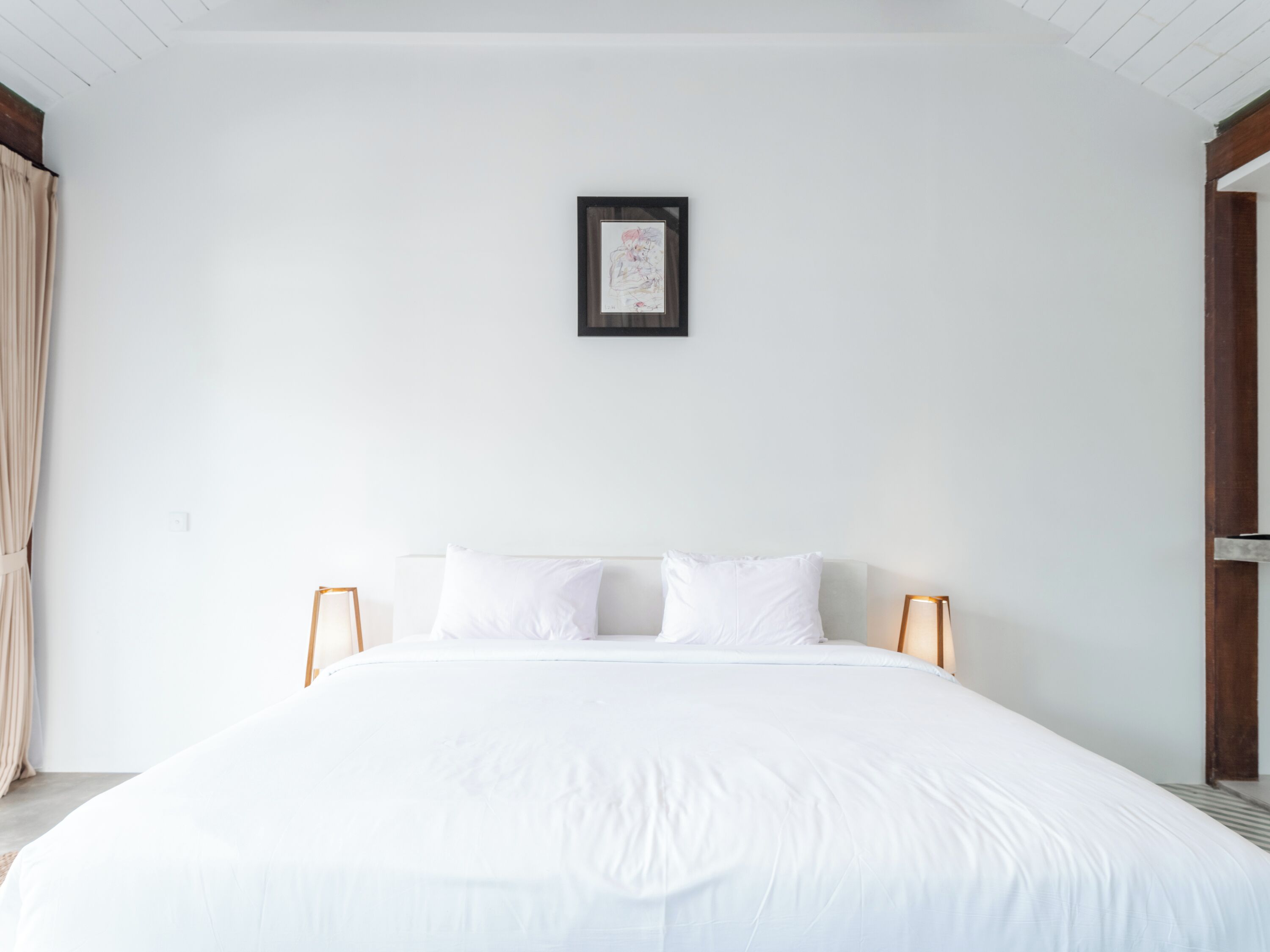 A bedroom with a large bed, white bedding, and a framed picture on the wall.