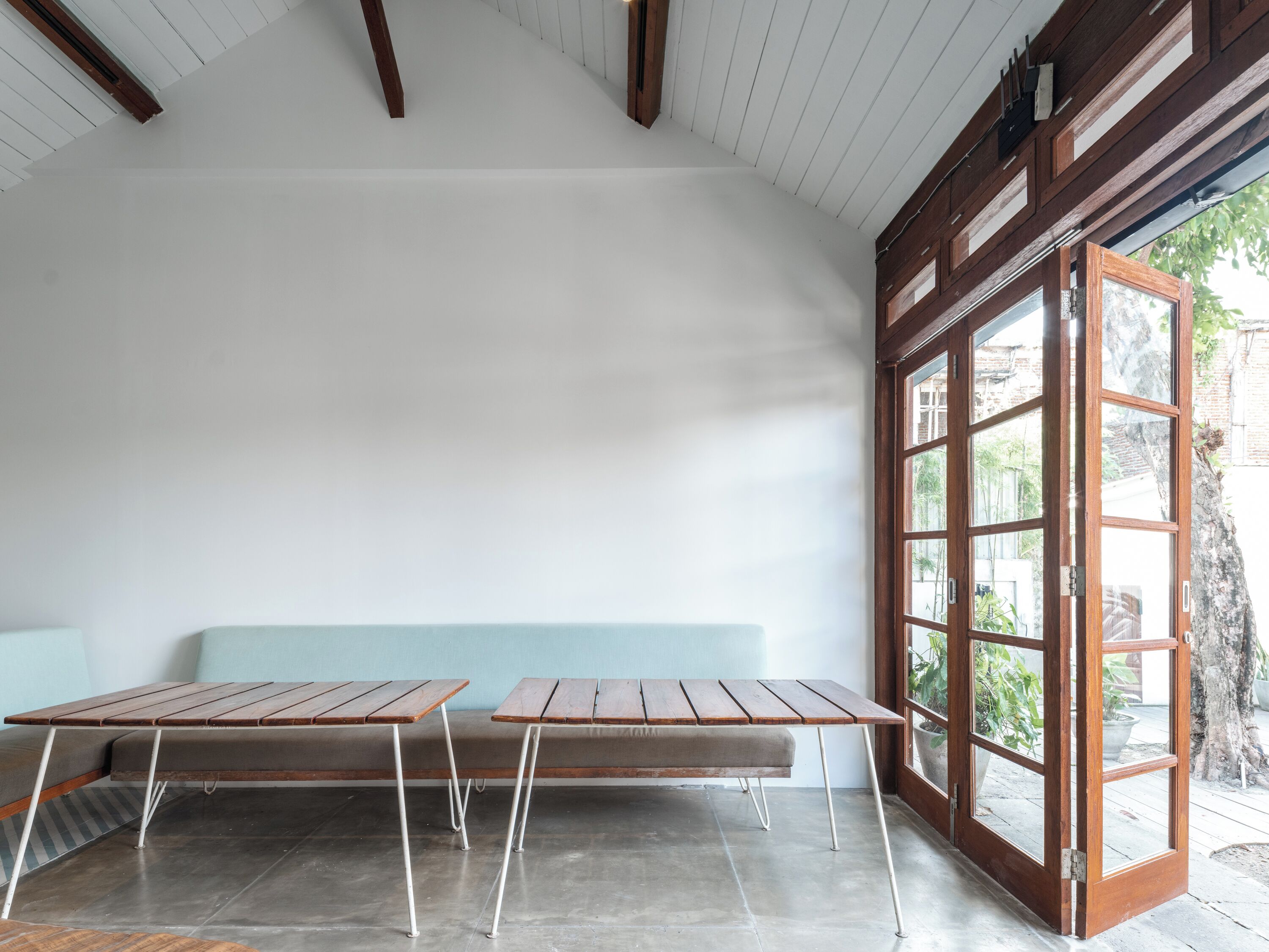 A room with two wooden tables and a bench, a large window, and a view of the outdoors.