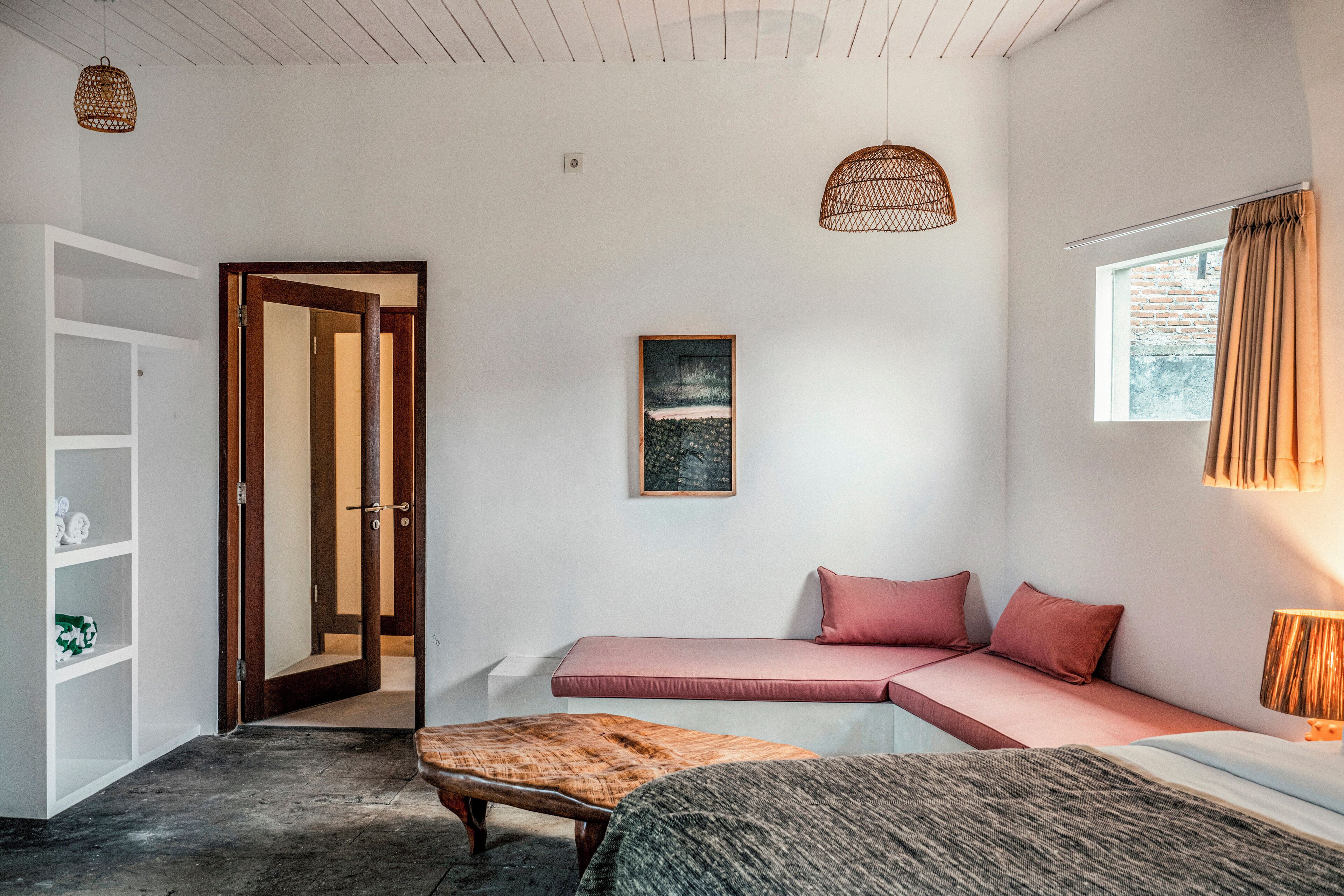 A bedroom with a built-in bench, a bed, a wooden bench, a picture on the wall, and a window with curtains.