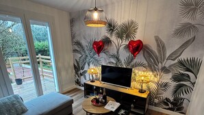 A modern living room with a sofa, a TV, and a small table with a bottle and glasses. - Agréable Maison au Calme , Proche de la mer (Meursac)
