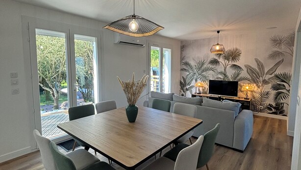 A modern dining area with a wooden table and chairs, a central vase, and a ceiling light fixture. - Agréable Maison au Calme , Proche de la mer (Meursac)