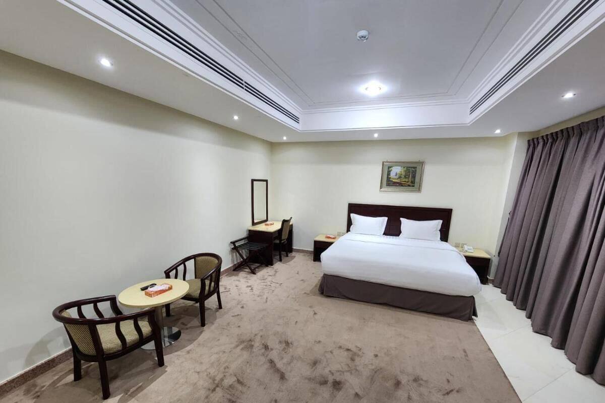 Een hotelkamer met een groot bed, een bureau met een stoel, een kleine ronde tafel met twee stoelen en een groot raam met gordijnen.