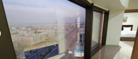 A hotel room with a large window offering a city view, a bed, and a small table.