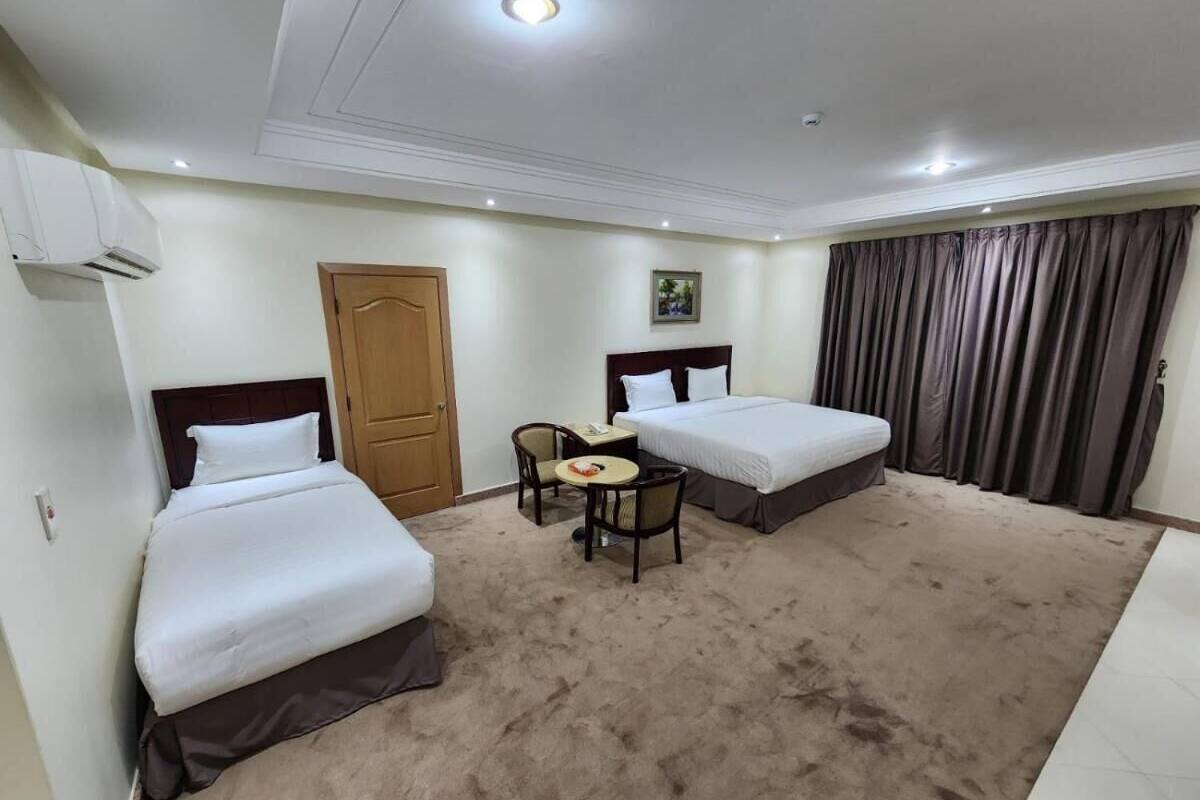 Een hotelkamer met twee bedden, een tafeltje met stoelen, een deur en een raam met gordijnen.