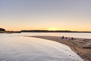 Une plage aux eaux calmes, avec peu de monde et des voiliers à l’horizon.