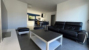 A modern living room with a black leather sofa, a white coffee table, and a dining area with a black and white table. - Maison 4ch/8pers Bourg de Baden, Proche des Plages au Coeur du Golfe du Morbihan (Baden)