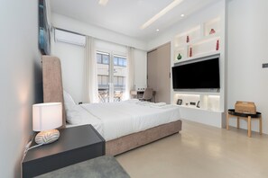 A modern hotel room with a large bed, a TV mounted on the wall, a desk with a lamp, and a view of the city through the window. - Minimal Studio with Balcony in Central Athens  (Athens)