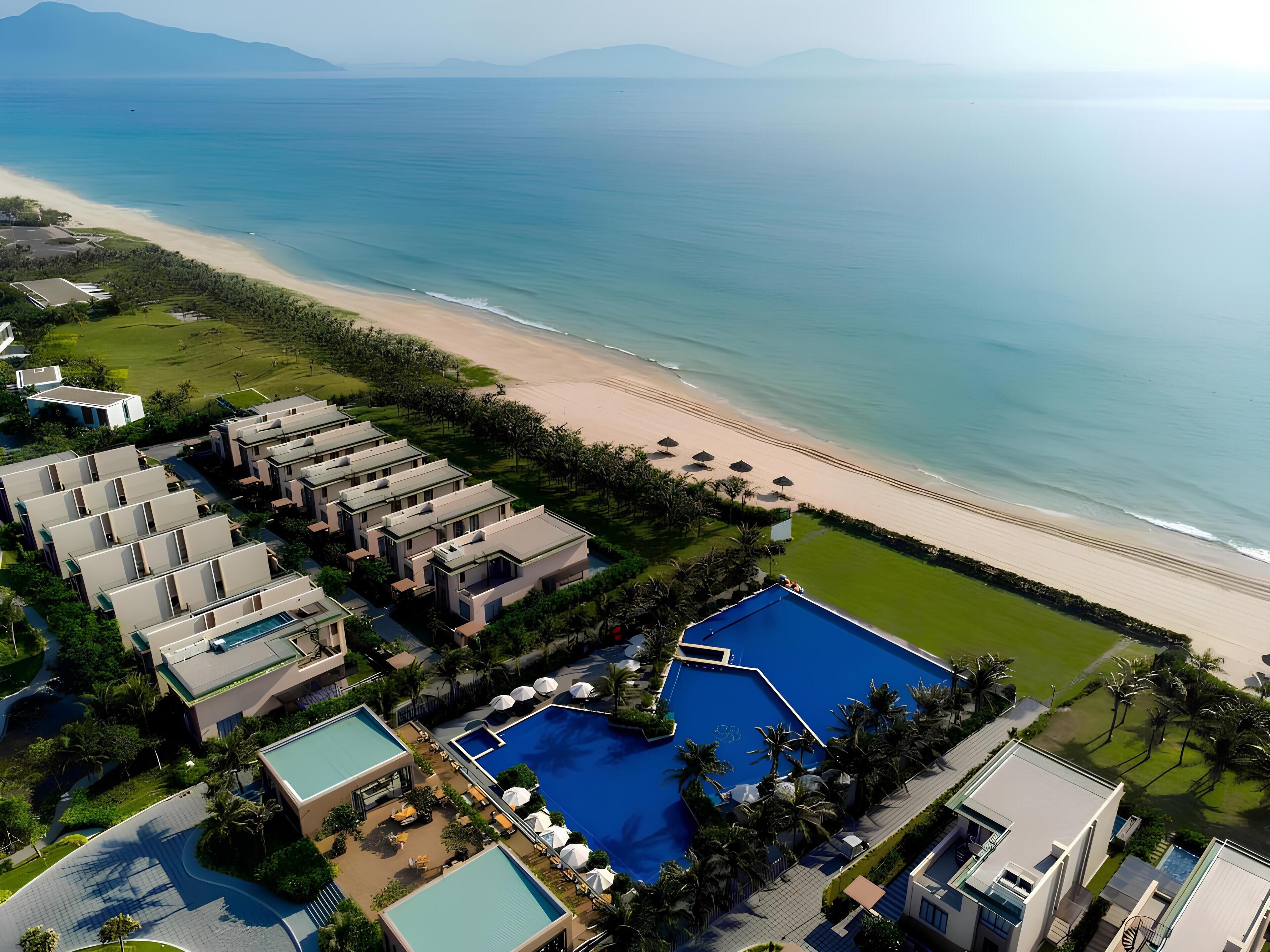 An aerial view of a resort with multiple buildings, a large swimming pool, and a beach.