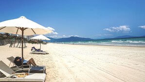 Een strand met ligbedden en parasols, een heldere lucht en de oceaan op de achtergrond.