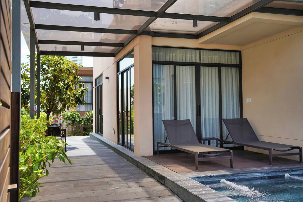 A modern outdoor pool area with two lounge chairs, a glass-enclosed patio, and a view of the cityscape.