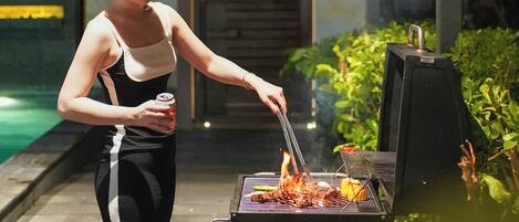 Iemand barbecuet buiten 's nachts, met een zwembad op de achtergrond.