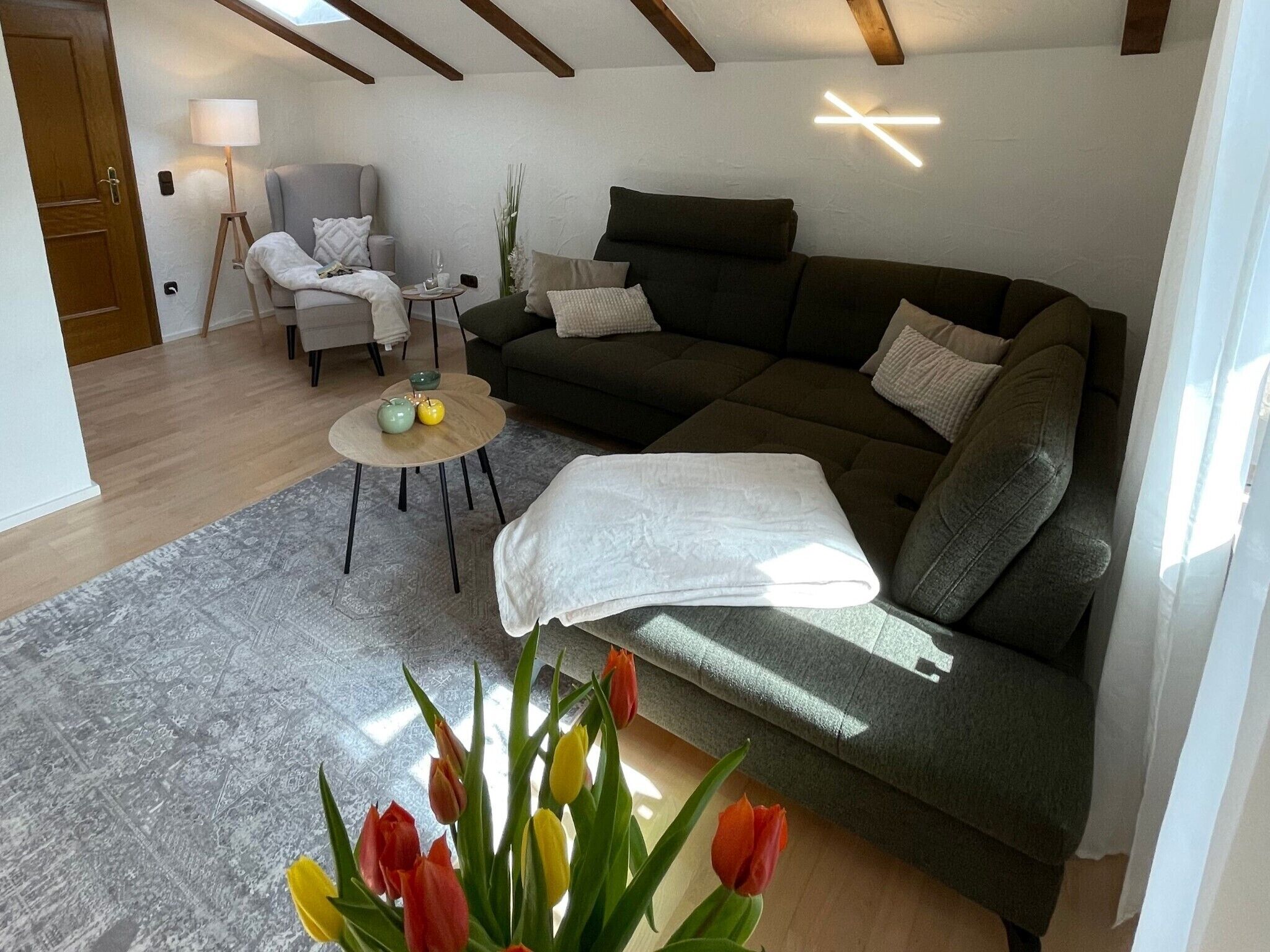 Een gezellige woonkamer met een bank, een klein rond tafeltje met een lamp en een vaas tulpen.