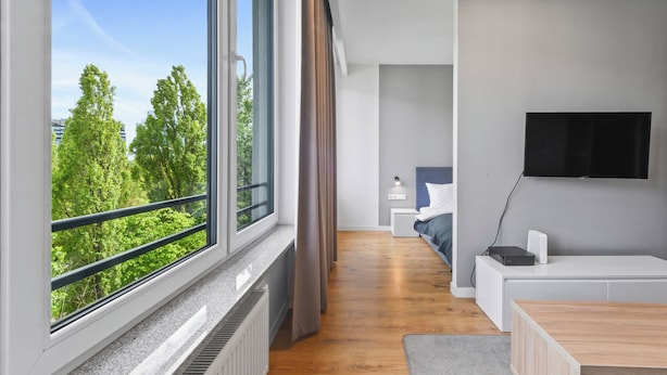 A modern hotel room with a large window, a flat-screen TV, a wooden floor, and a seating area with a small table. - RentPlanet - Apartamenty Sławińska (Warsaw)