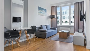 A modern living room with a sofa, chairs, a coffee table, a TV mounted on the wall, and a window with curtains. - RentPlanet - Apartamenty Sławińska (Warsaw)