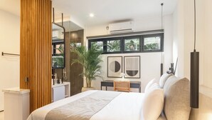 Un dormitorio moderno con una cama grande, un separador de madera, un escritorio con una silla, una planta en maceta y obras de arte en la pared.
