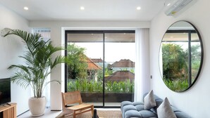 Una sala de estar moderna con un gran ventanal corredero, un sofá azul, una silla de madera, un televisor y una planta en maceta.