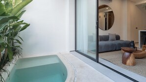 Una sala de estar moderna con un ventanal que da a un balcón, un sofá gris y una pequeña mesa de madera.