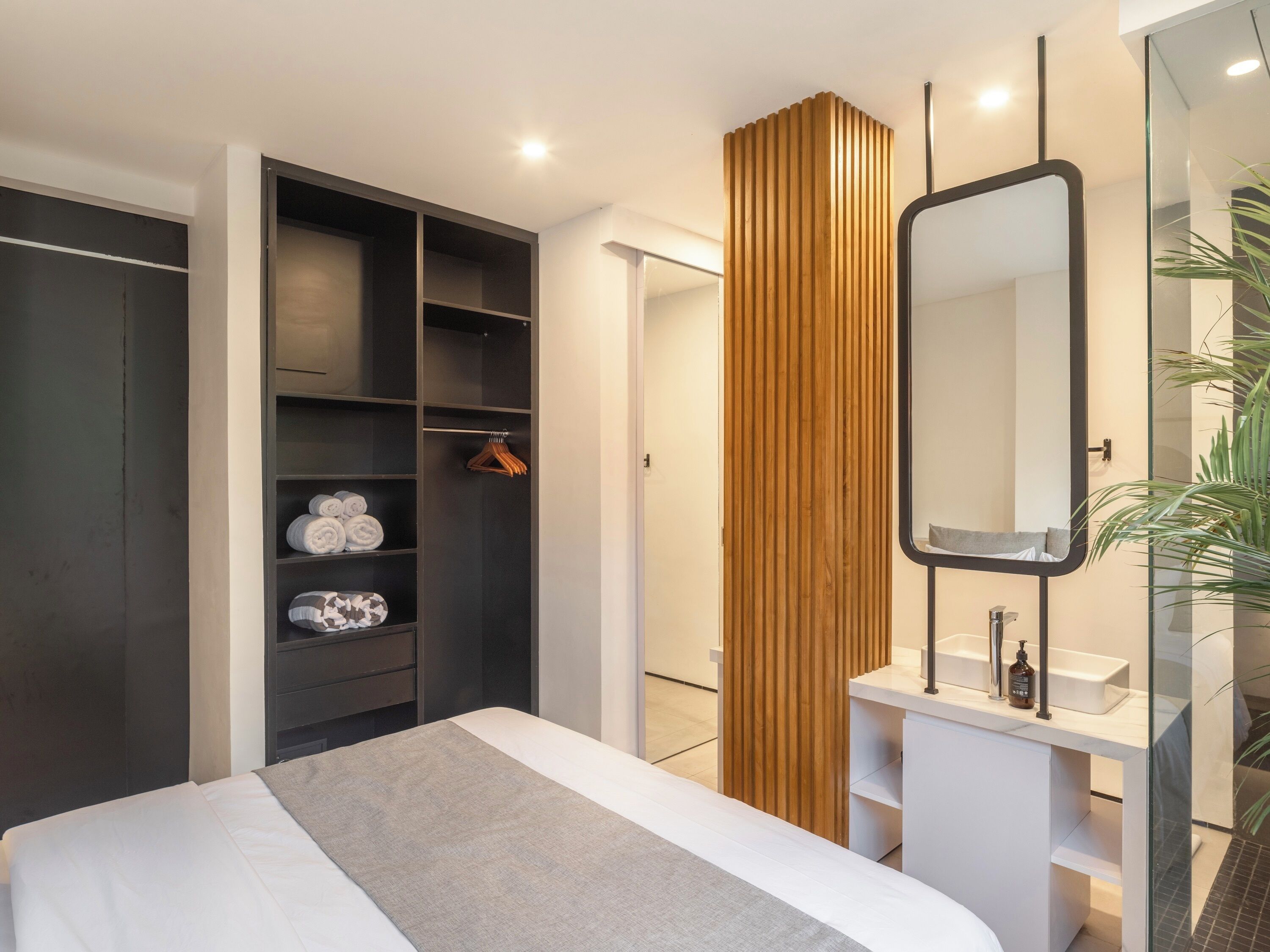 A modern bedroom with a large bed, a wardrobe, a wooden panel, a mirror, and a bathroom with a sink and mirror.