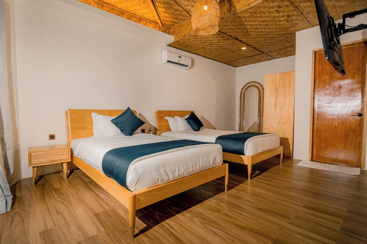 Quarto com duas camas de madeira, teto e piso de madeira.