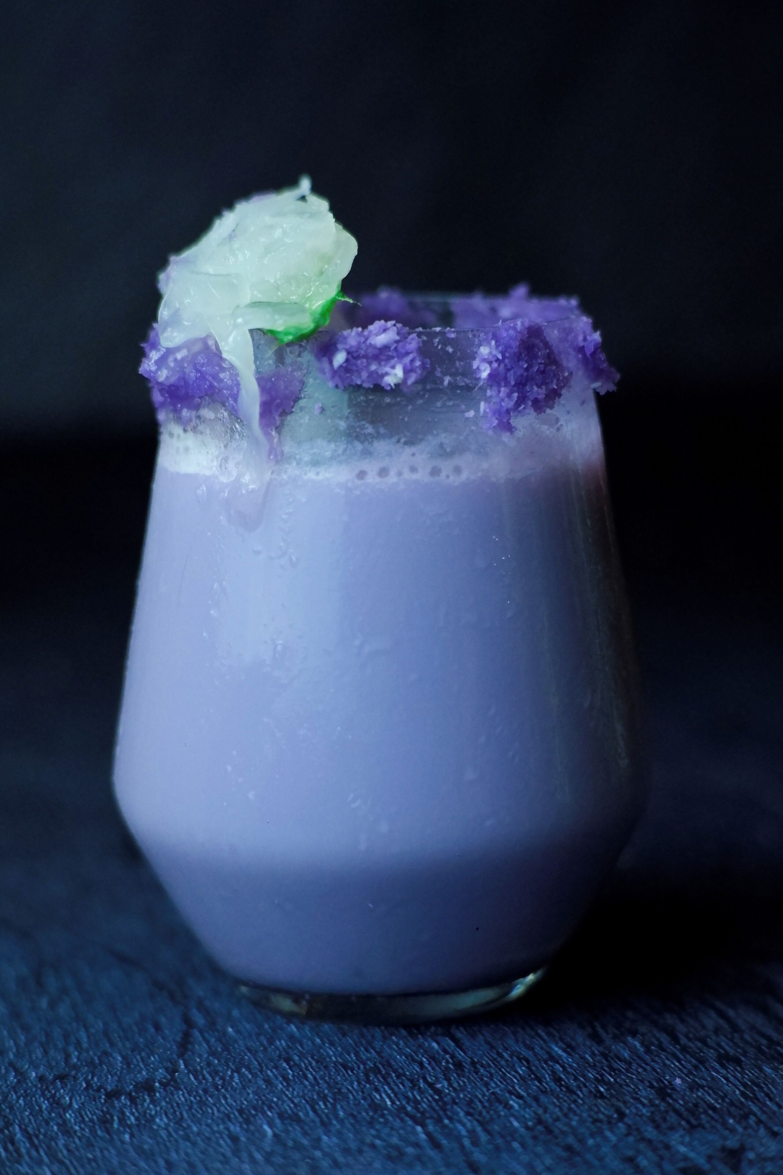 Un vaso con bebida morada, adornado con una lima y cristales morados.