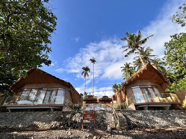 A resort with thatched-roof buildings, palm trees, and a clear blue sky. - Nadhibar Resort (Mahinog)