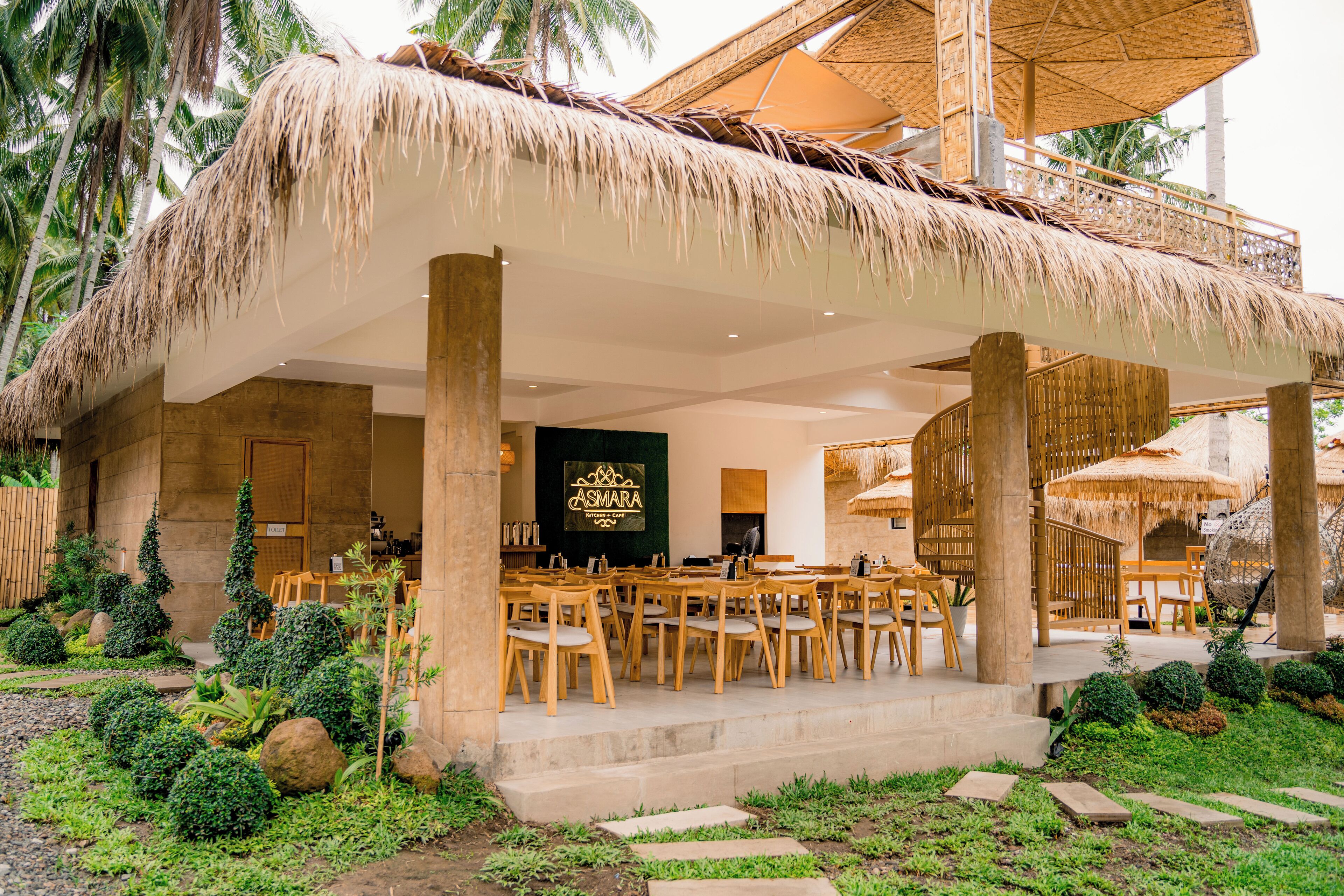 Un área de comedor al aire libre con techo de paja y asientos, y un letrero que dice "ASWARA".