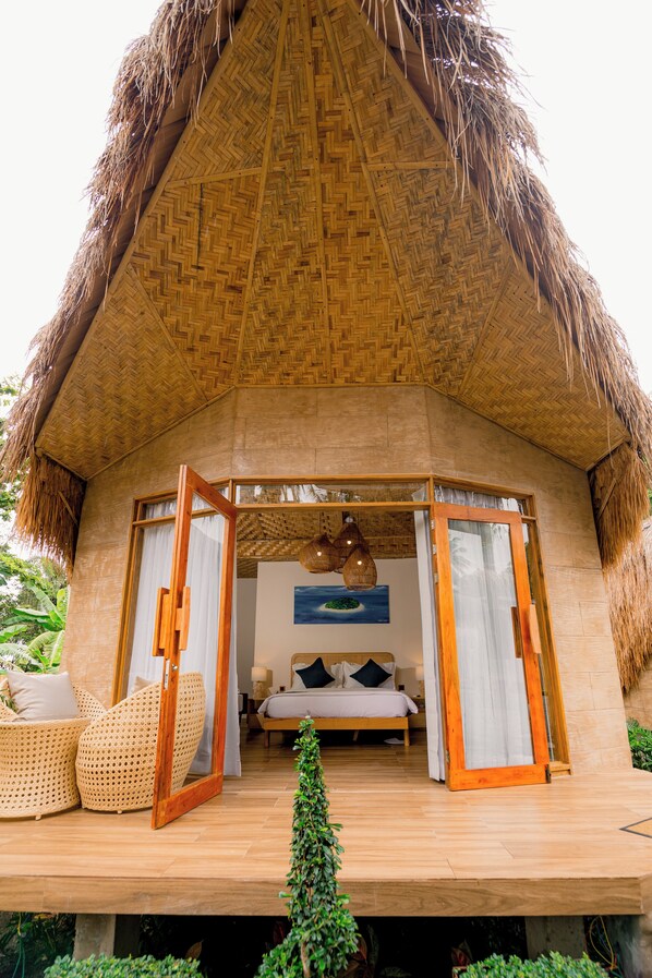 A thatched-roof bungalow with a wooden deck, a bed with white linens, and wicker furniture. - Nadhibar Resort (Mahinog)