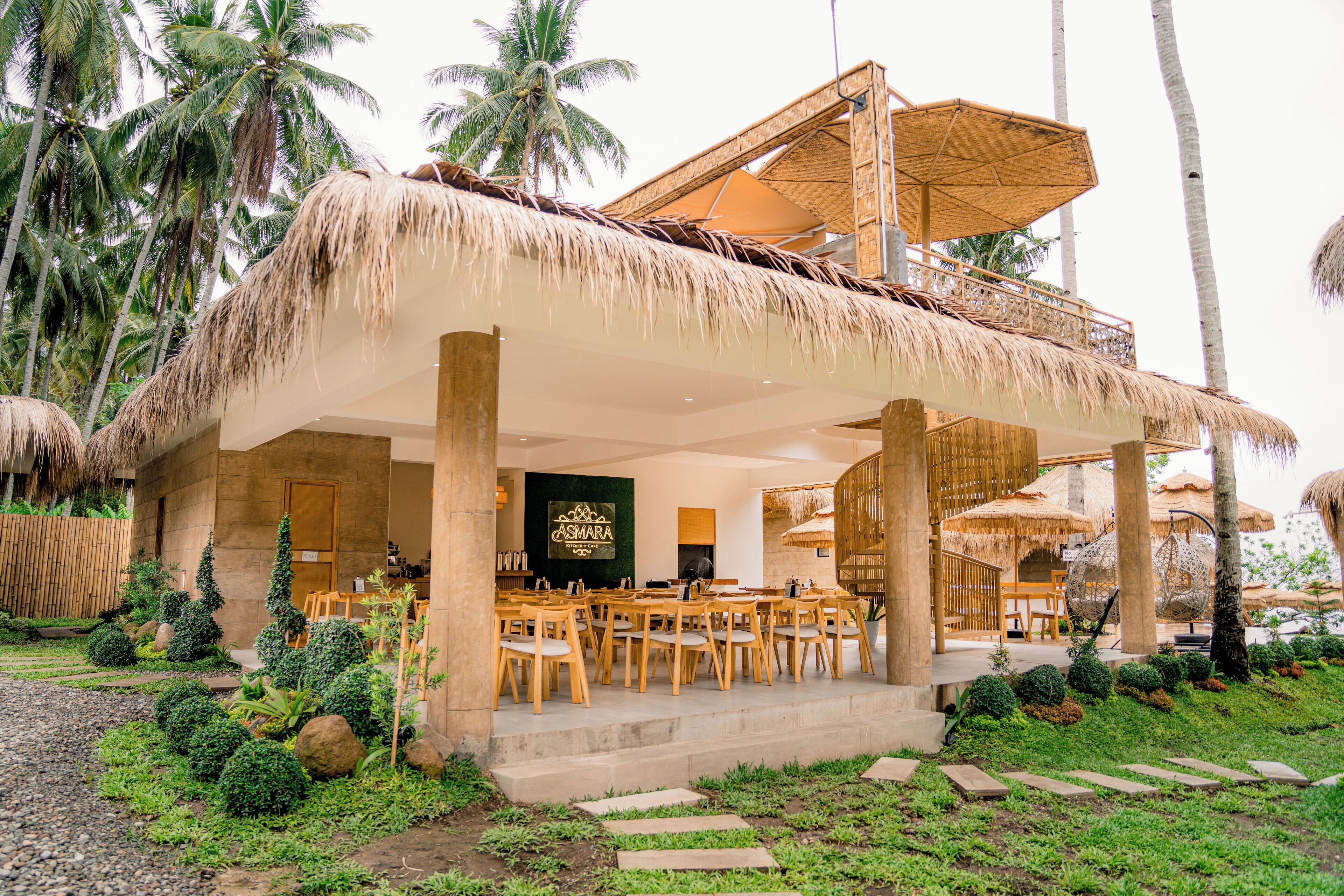 A resort with a thatched-roof outdoor dining area, palm trees, and a sign reading "ASMARA".