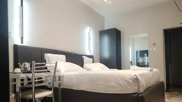 A modern hotel room with a bed, a desk with a chair, a mirror, and a television. - Triple Tee Luxury Hotel (Lagos)