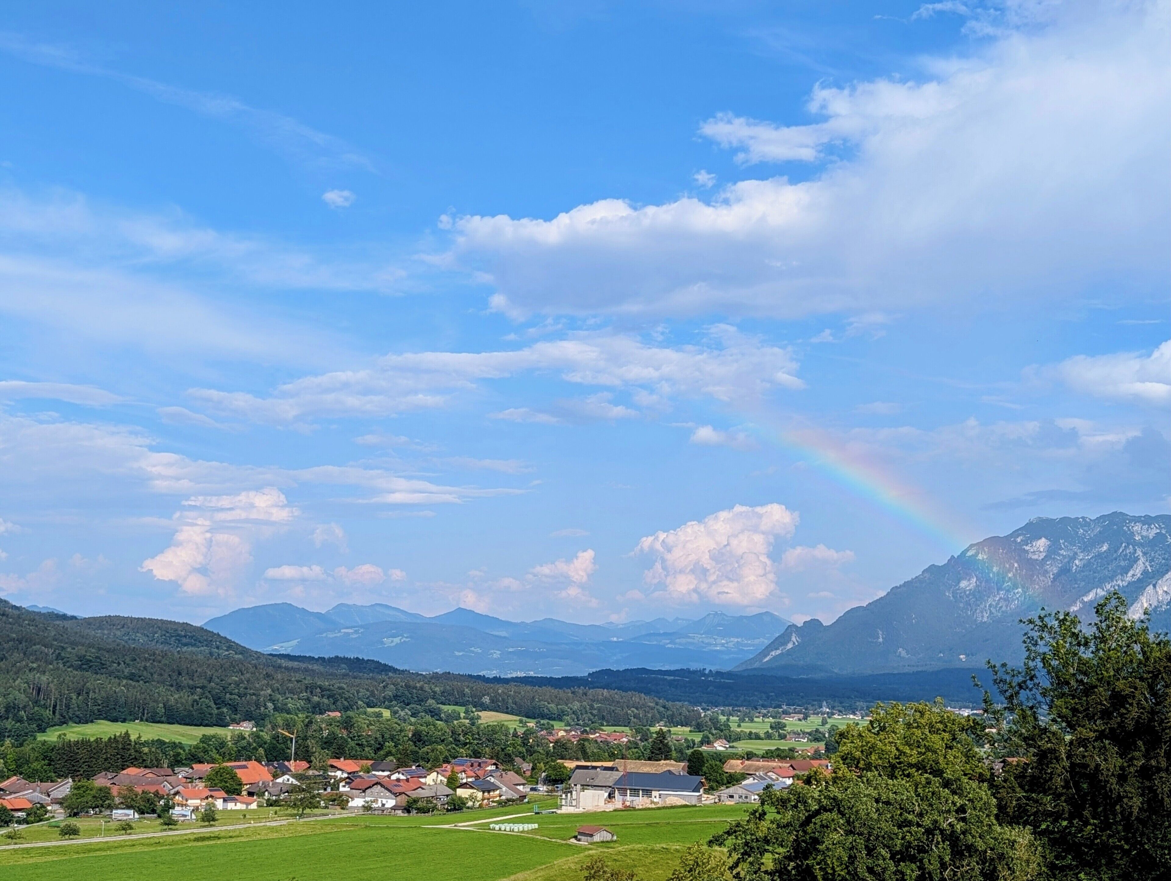 A rural landscape with a village, mountains, and a rainbow.