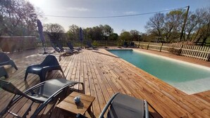 A wooden deck with a pool, lounge chairs, and a table. - Gîte Laurence 4/5 Personnes (Rogues)