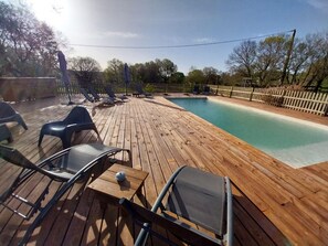 Une terrasse en bois avec une piscine, des chaises longues et une table.