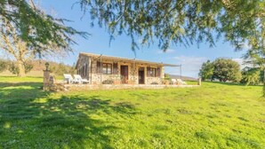 Un bâtiment rustique en pierre, doté d’un porche et entouré d’une pelouse verdoyante.