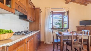 Une cuisine avec des meubles en bois, une cuisinière à gaz, une table à manger avec des chaises et une fenêtre donnant sur un paysage verdoyant.
